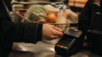 A hand in a winter coat taps a card at a grocery checkout terminal.