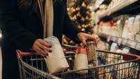 Hands place baking ingredients into a cart in a holiday-decorated aisle.