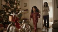 Maya runs toward a new bicycle under the Christmas tree while Adrianna watches from the doorway.